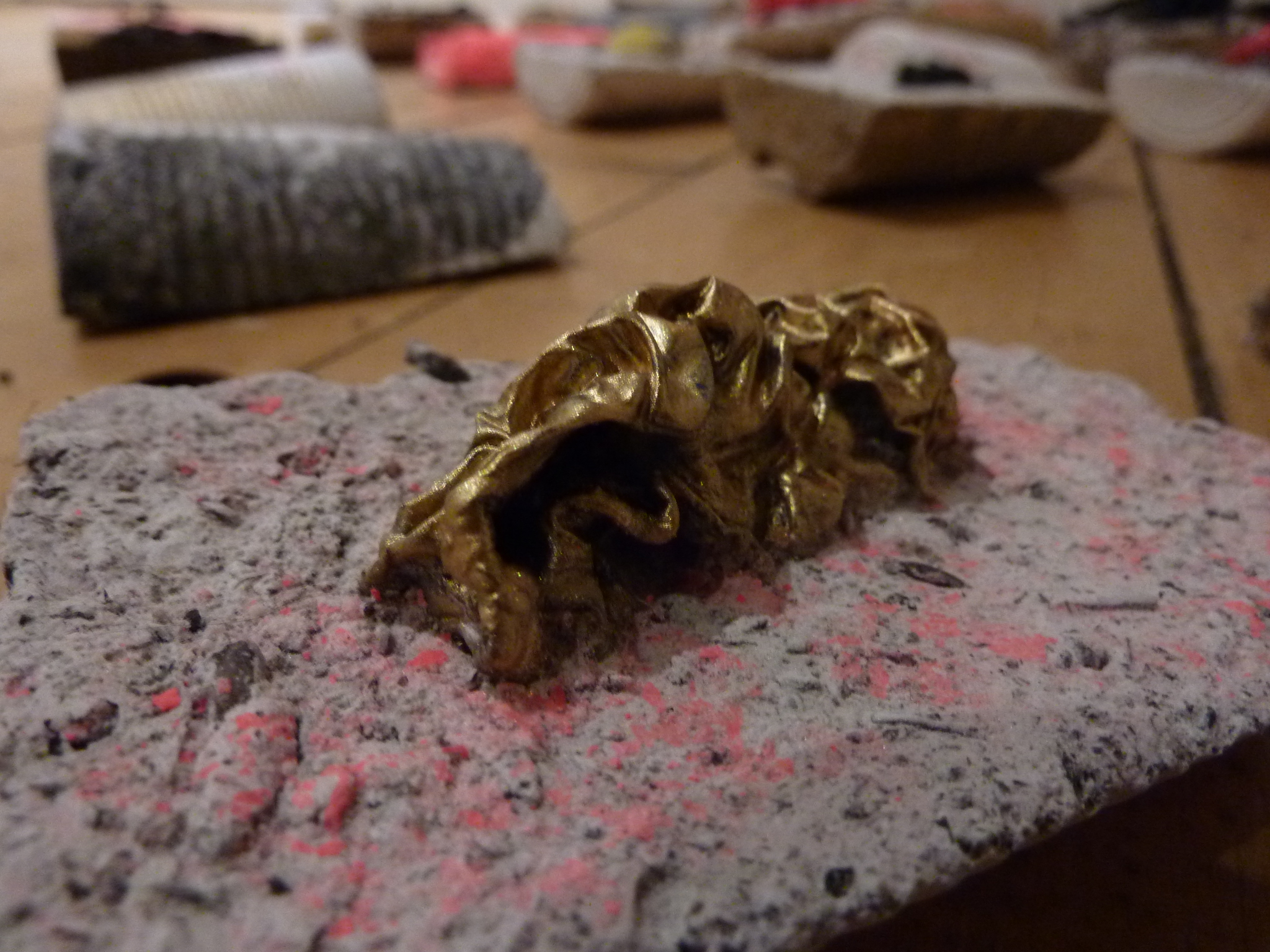 25. Anthropocene fragments (circa 1950–2020 AD) — Close-up: gold-coloured organic form embedded in plaster