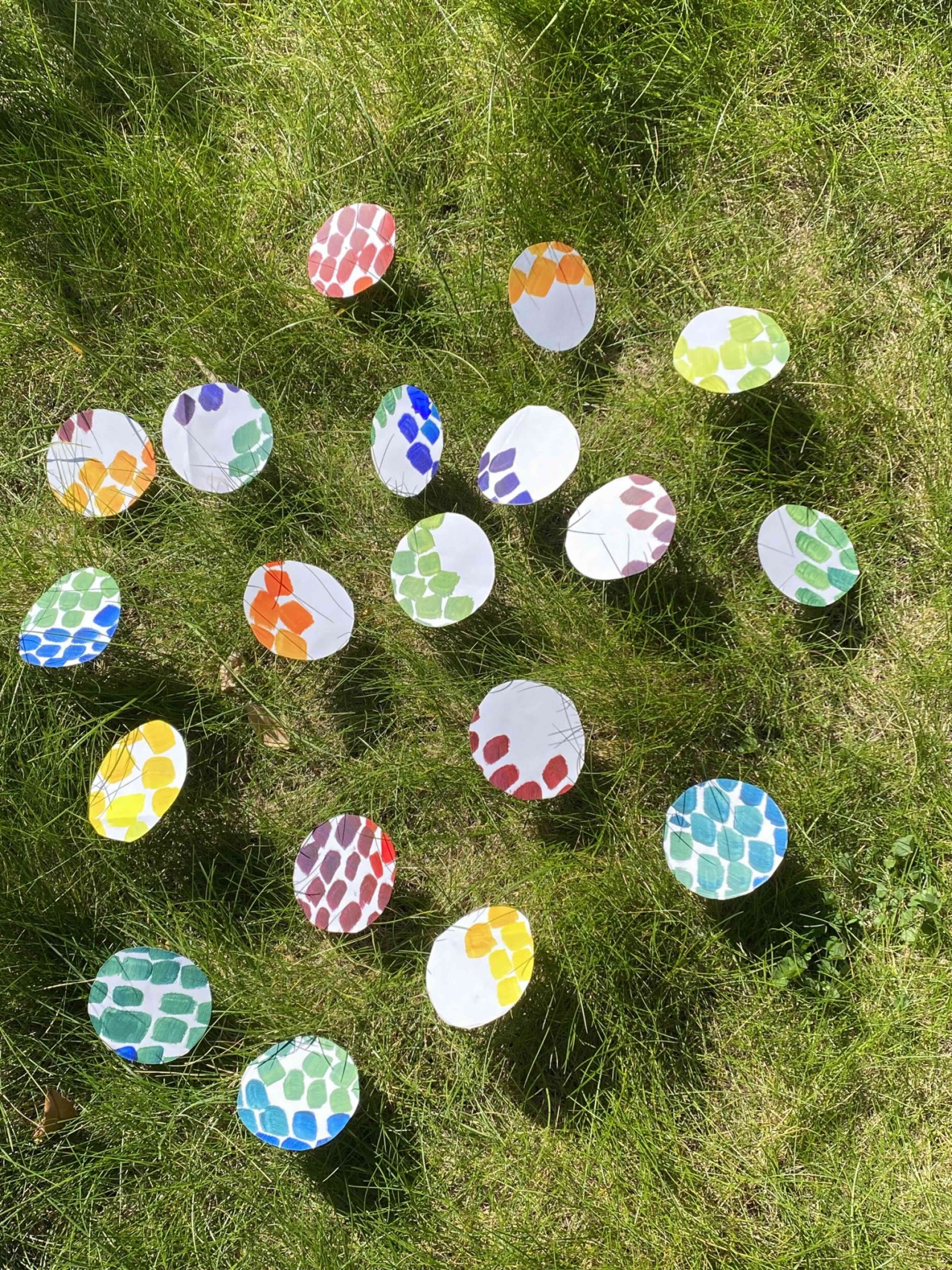 Hand-painted paper circles in many colours scattered across green grass.